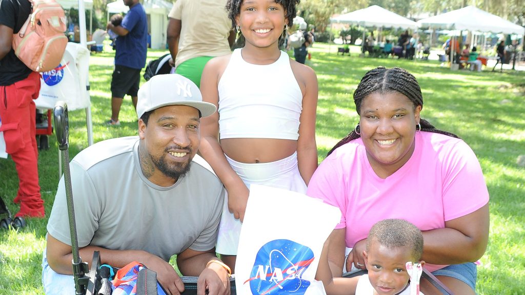 A family of four event-goers pause and smile with their wagon filled with event giveaways