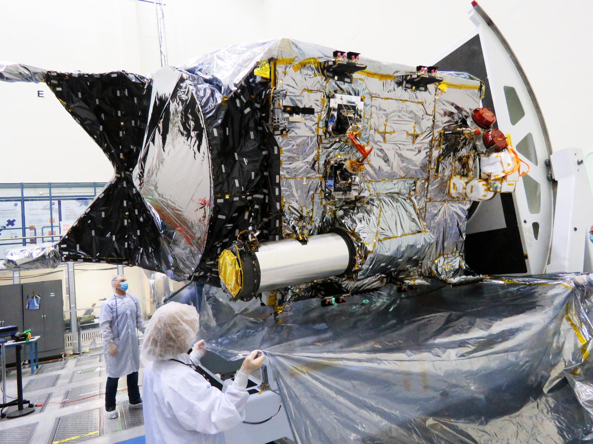 The Deep Space Optical Communications (DSOC) technology demonstration's flight laser transceiver is seen attached to NASA's Psyche spacecraft inside a clean room at the agency's Jet Propulsion Laboratory in Southern California. DSOC's tube-like gray/silver sunshade can be seen protruding from the side of the spacecraft. The bulge to which the sunshade is attached is DSOC's transceiver, which consists of a near-infrared laser transmitter to send high-rate data to Earth and a sensitive photon-counting camera to receive ground-transmitted low-rate data.