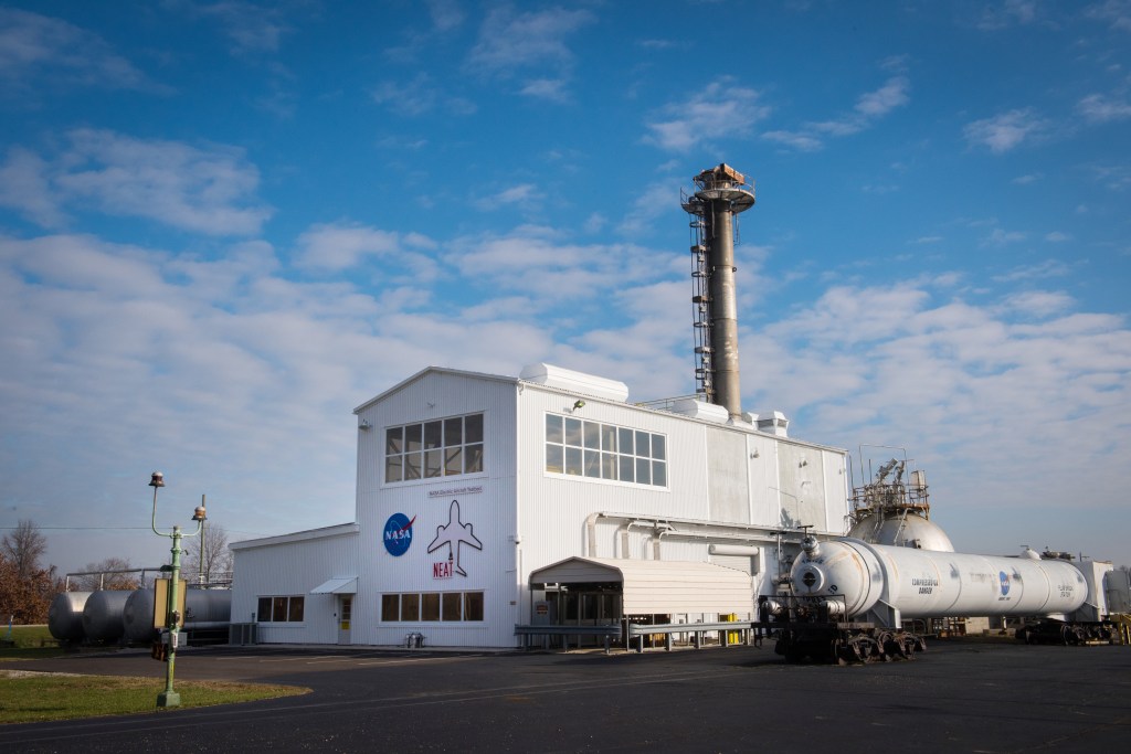 A white building surrounded by external equipment in front of a blue sky with clouds.