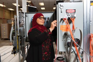 A woman accesses the inside of a testing machine connected to wires inside the facility.