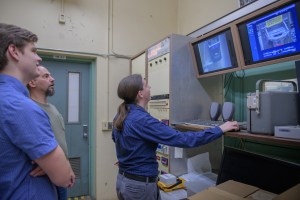 Three men face away from the camera viewing data on monitors inside a testing facility. 