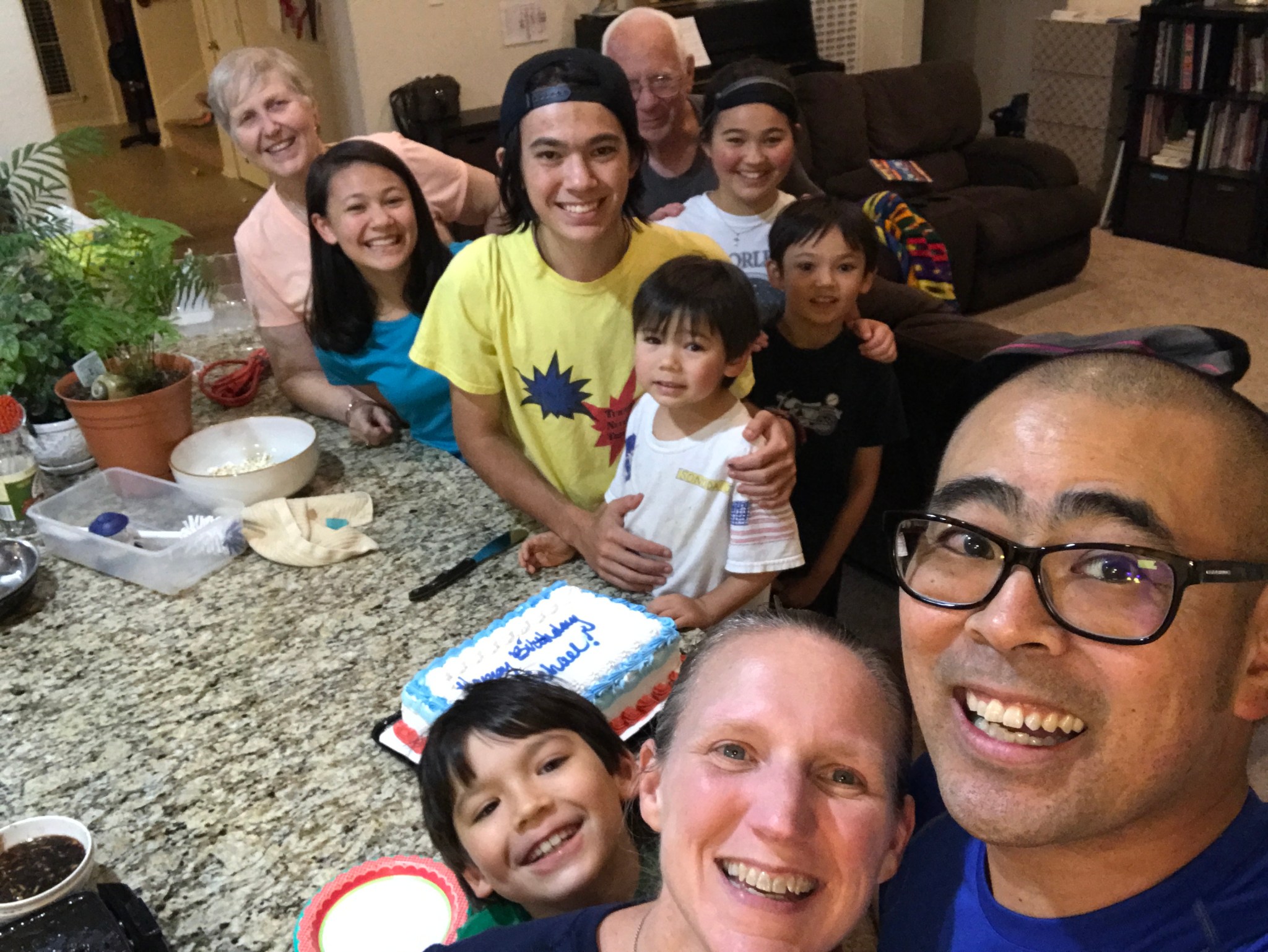 A family gathers around a kitchen island, smiling for a group photo. 