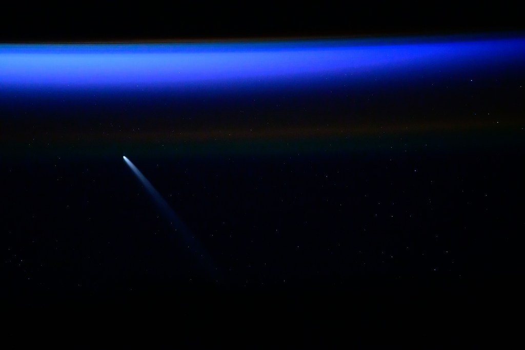 Dark background of the sky with bright blue horizon color and comet pictured from the International Space Station as it orbited 271 miles above the South Atlantic Ocean.