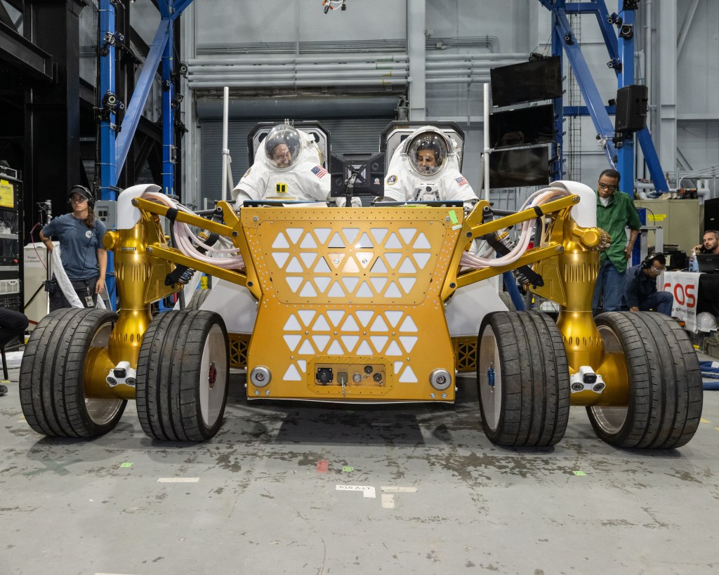 Suited NASA engineers sit on the rover prototype during testing at NASA’s Johnson Space Center in Houston.