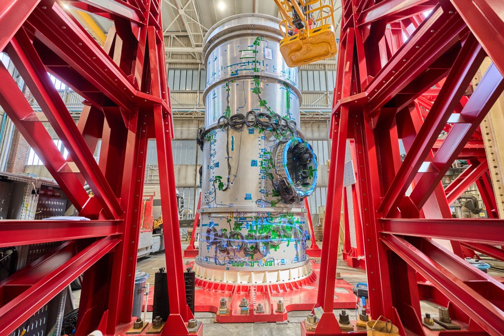 Gateway’s Habitation and Logistics Outpost (HALO) is seen standing vertically inside a Thales Alenia Space facility in Turin, Italy. The cylindrical metallic module is surrounded by a red steel frame. Thales Alenia Space is the subcontractor for Northrop Grumman, NASA's commercial partner developing HALO. Photo Credit: Thales Alenia Space.