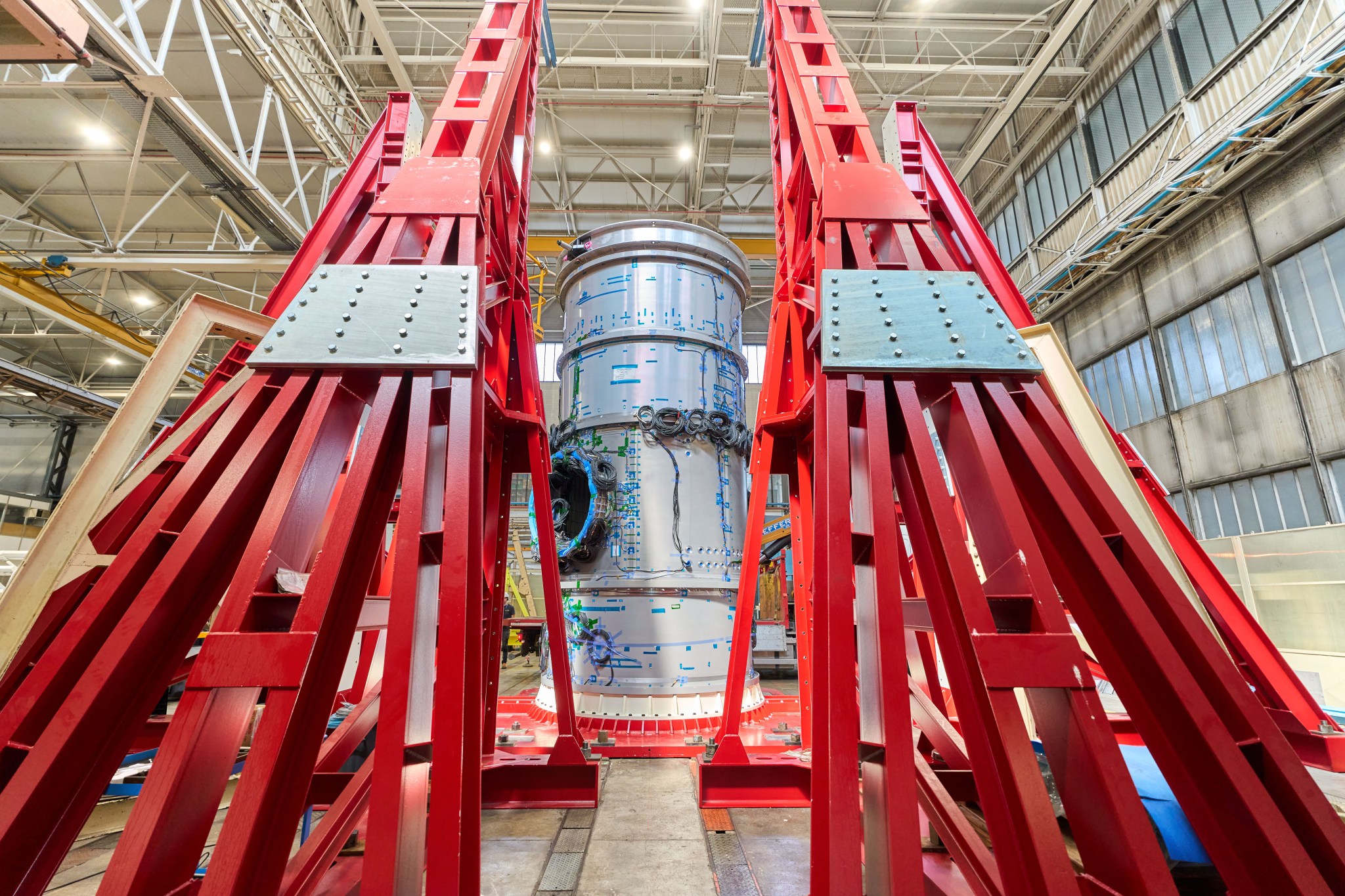 Gateway’s Habitation and Logistics Outpost (HALO) is seen standing vertically inside a Thales Alenia Space facility in Turin, Italy. The cylindrical metallic module is surrounded by a red steel frame. Thales Alenia Space is the subcontractor for Northrop Grumman, NASA's commercial partner developing HALO. Photo Credit: Thales Alenia Space.