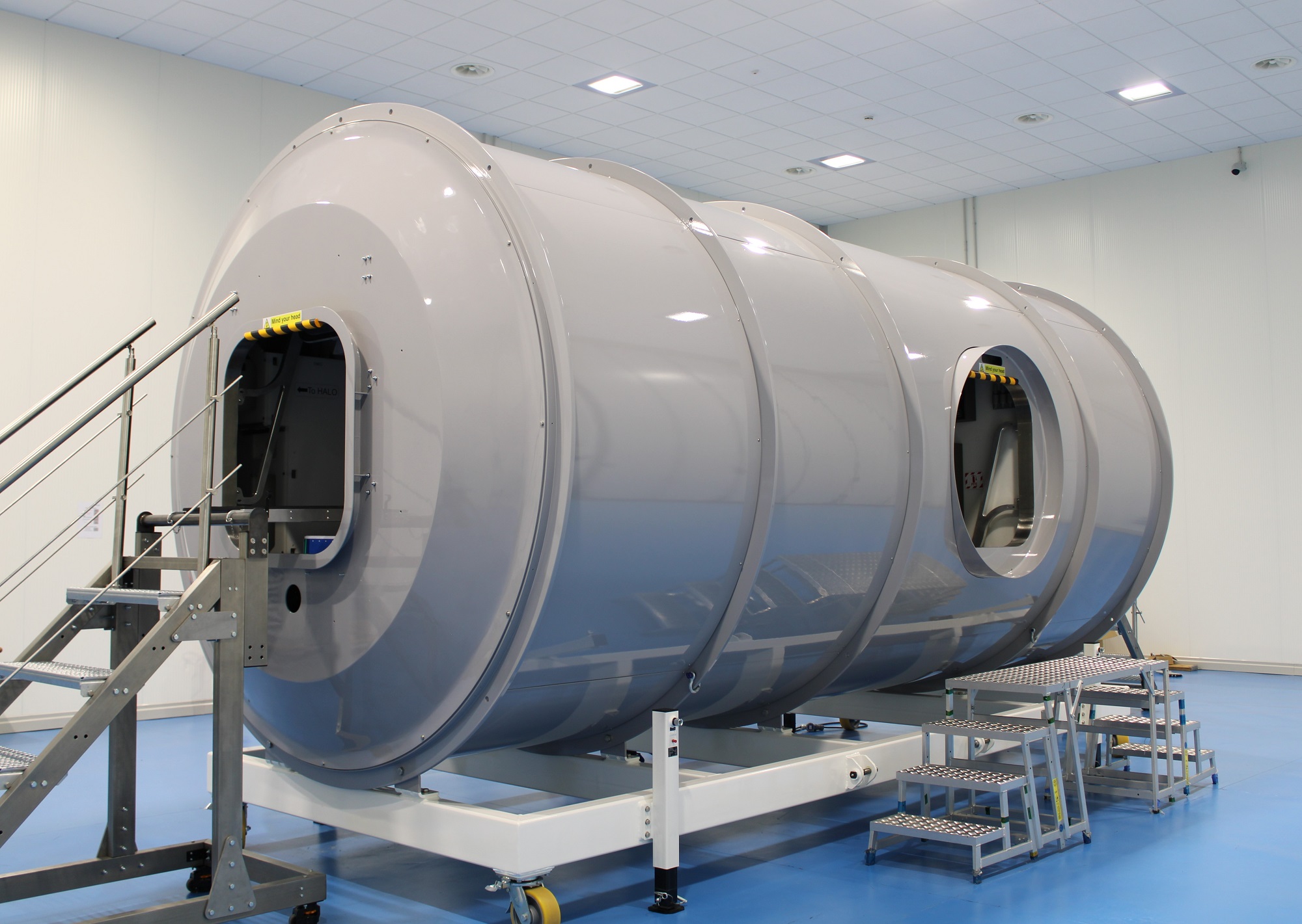 Full-scale mock-up of ESA’s Lunar I-Hab habitation module for Gateway. The cylindrical structure is set up in a testing facility, with stairs leading to access points on the module. Engineers use this low-fidelity model to finetune interior design for astronaut safety and functionality.