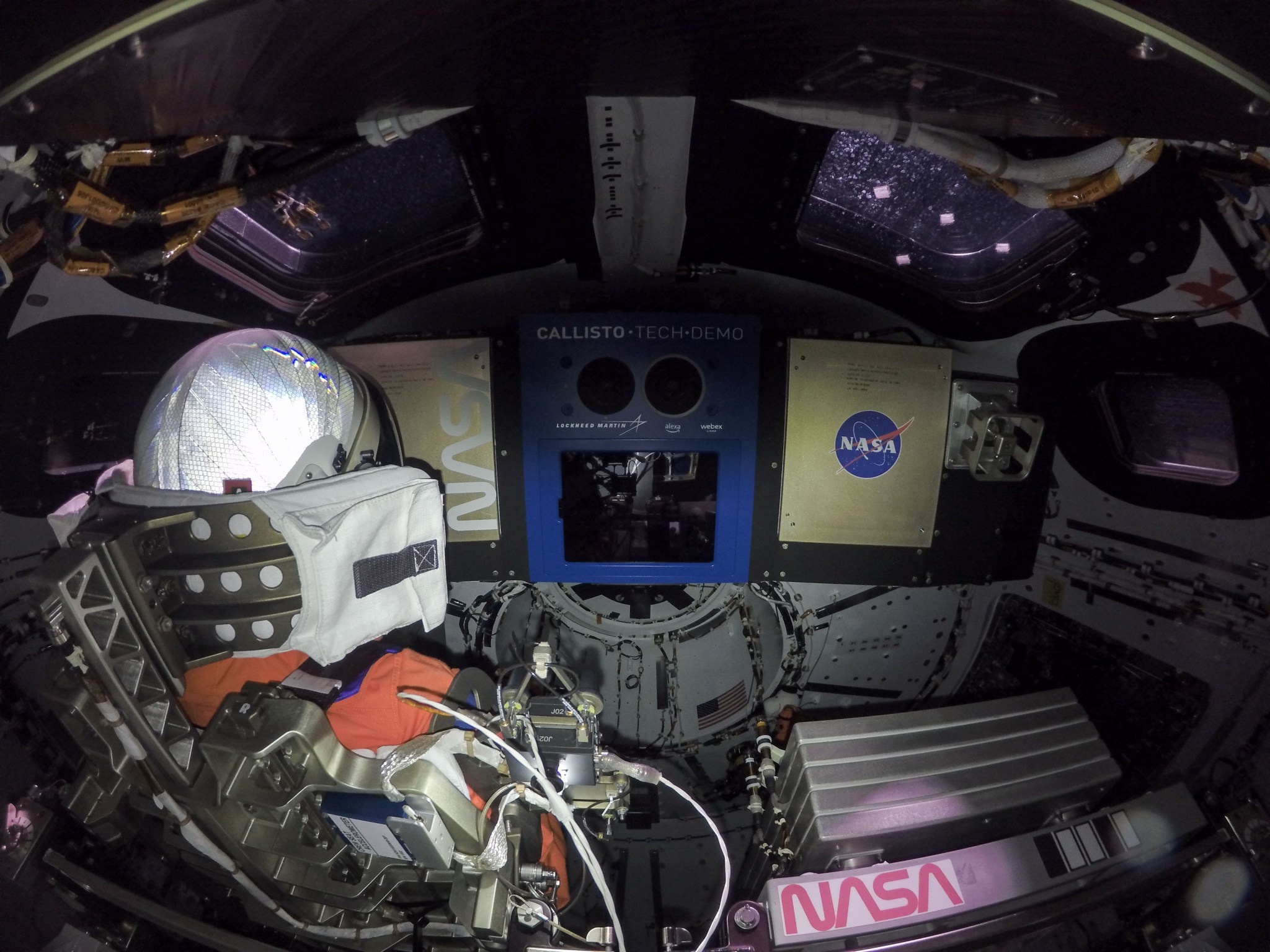 An orange manikin is pictured seated inside of the Orion capsule.