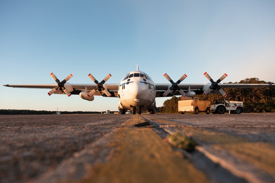 A C-130 aircraft with four propellors is parked on the yellow painted lines of an airfield.