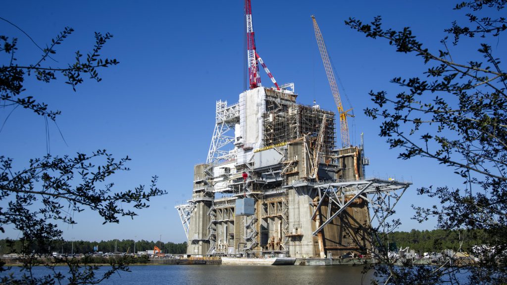 A view of Thad Cochran Test Stand (B-1/B-2) from across a small body of water is shown with a crane in the background