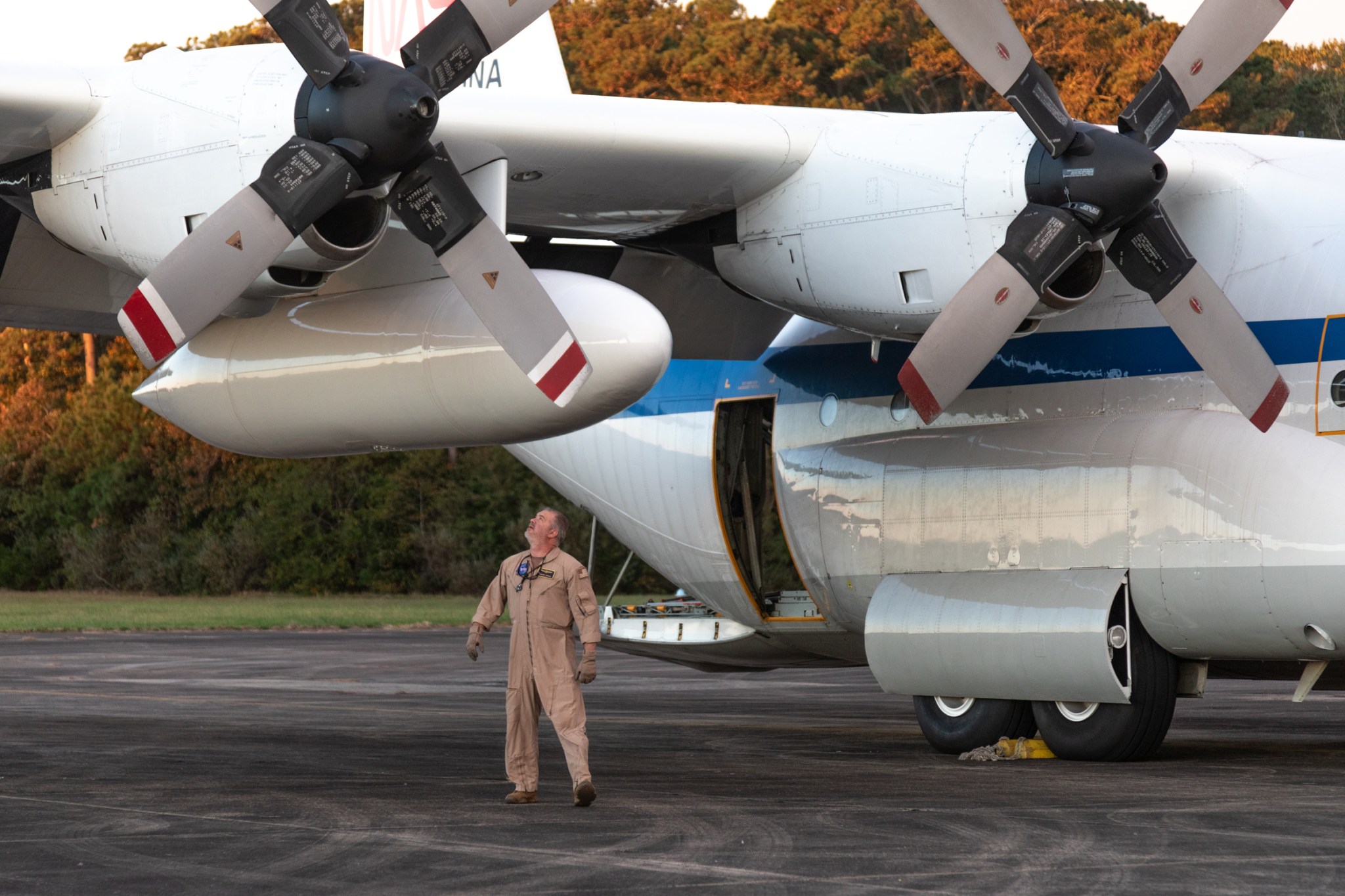 A member of the flight crew stands underneath the large wing of the C-130, looking up to inspect it prior to departure.