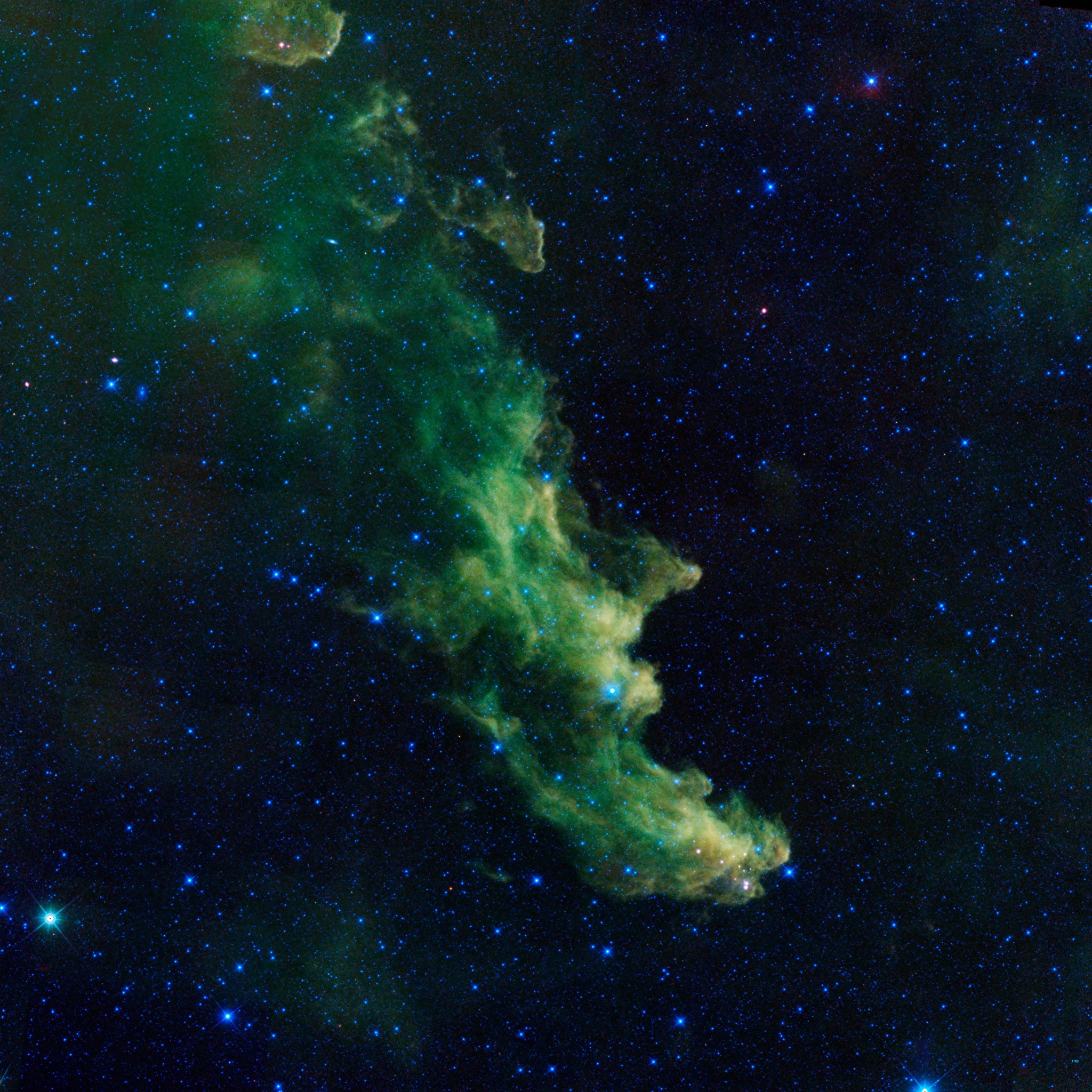 A green nebula looks like a witch's head looking to the right of the image. There is a pronounced "nose" and "chin." Blue stars are around and in the green clouds.