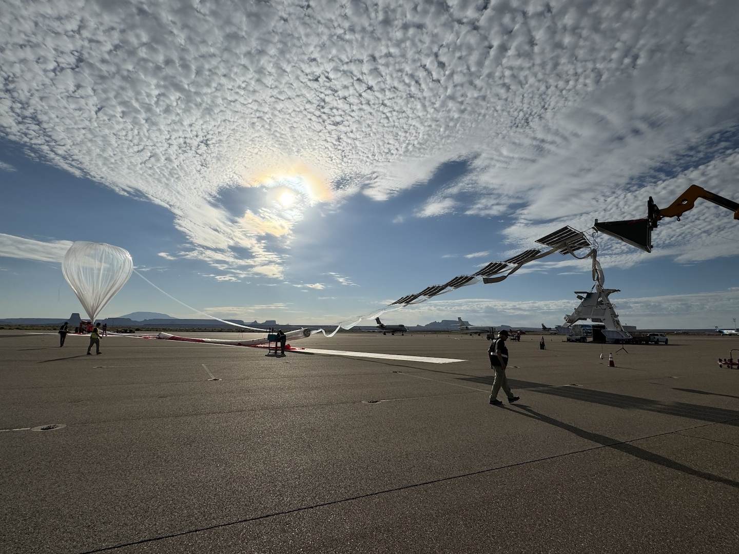 A high-altitude balloon with tethered payload sits on the launching ground.