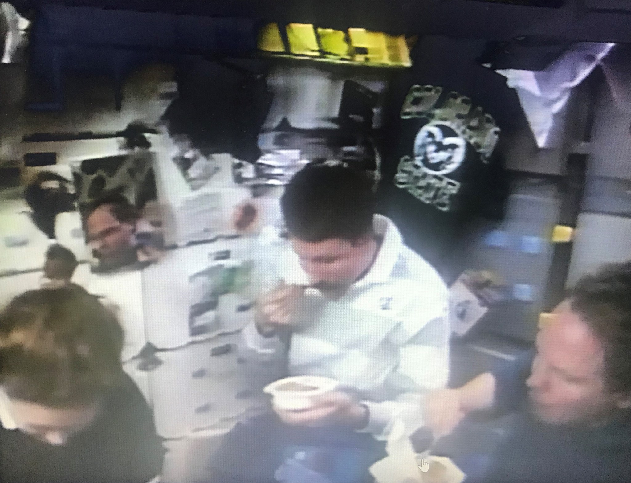 An astronaut in a white shirt is eating Thanksgiving dinner onboard a spacecraft with two other astronauts.