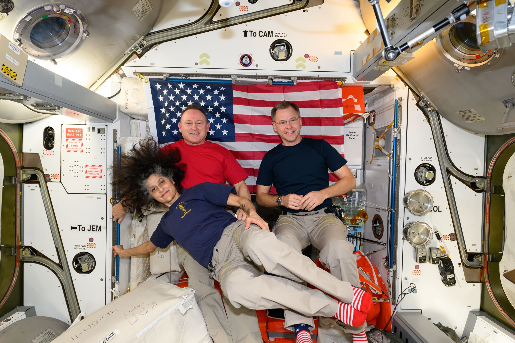 Expedition 72 Commander Suni Williams and Flight Engineers Butch Wilmore and Nick Hague, all three NASA astronauts, pose for a portrait together with the U.S. flag behind them aboard the International Space Station's Harmony module. The trio was honoring veteran members of the U.S. Armed Forces during Veterans Day. Williams is a retired U.S. Navy captain, Wilmore is a U.S. Navy test pilot, and Hague is U.S. Space Force colonel.