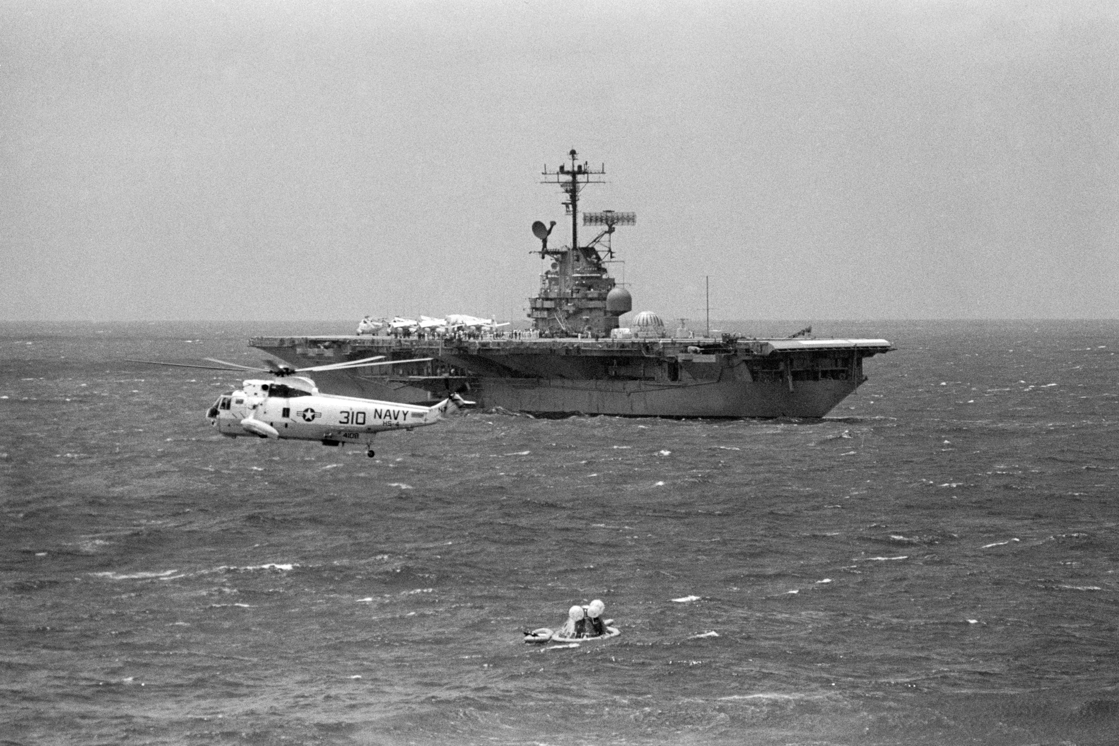 Apollo 12 Command Module Yankee Clipper in the water with U.S.S. Hornet approaching as a rescue helicopter circles