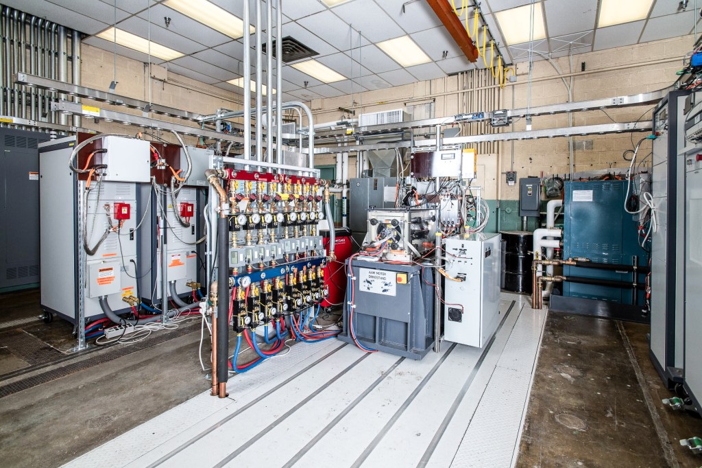 A room full of various testing equipment, including gauges, cables, and machinery, with a rectangular motor drive stand in the center.