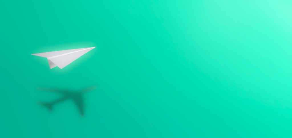 Image of a paper airplane floating over a shadow of an airplane on a green background