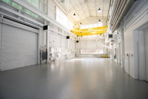 The inside of a large building with a high ceiling with hanging lights, white walls, and open floor space.