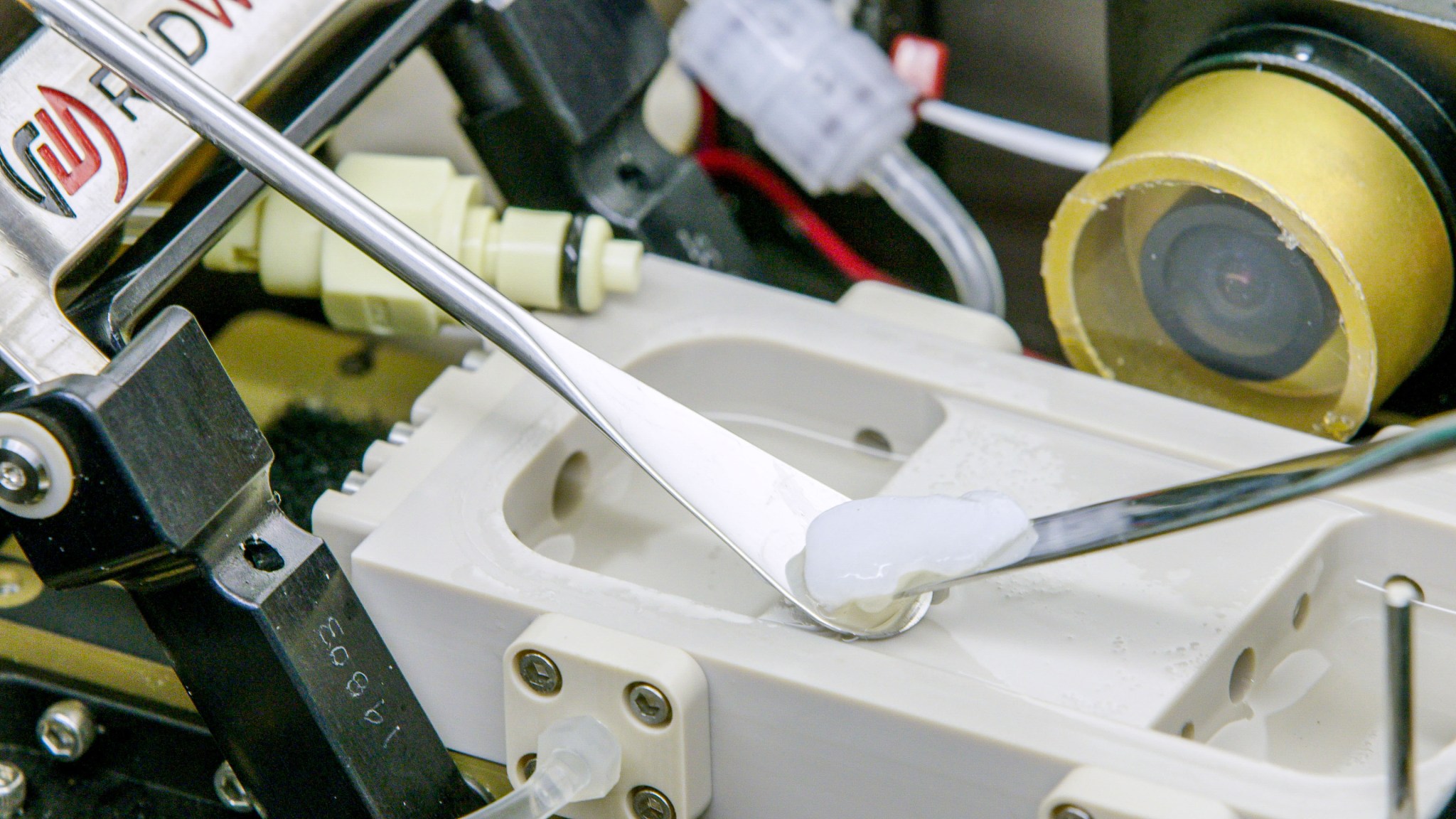 A close-up of a scientific instrument. The setup includes metal spatulas and a sample of a substance placed in a specialized container.