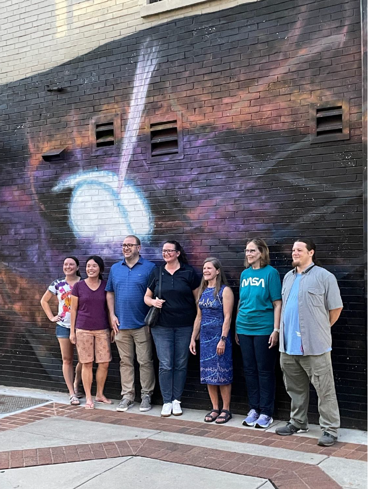 Scientists stand before an outdoor mural in Huntsville, Alabama.