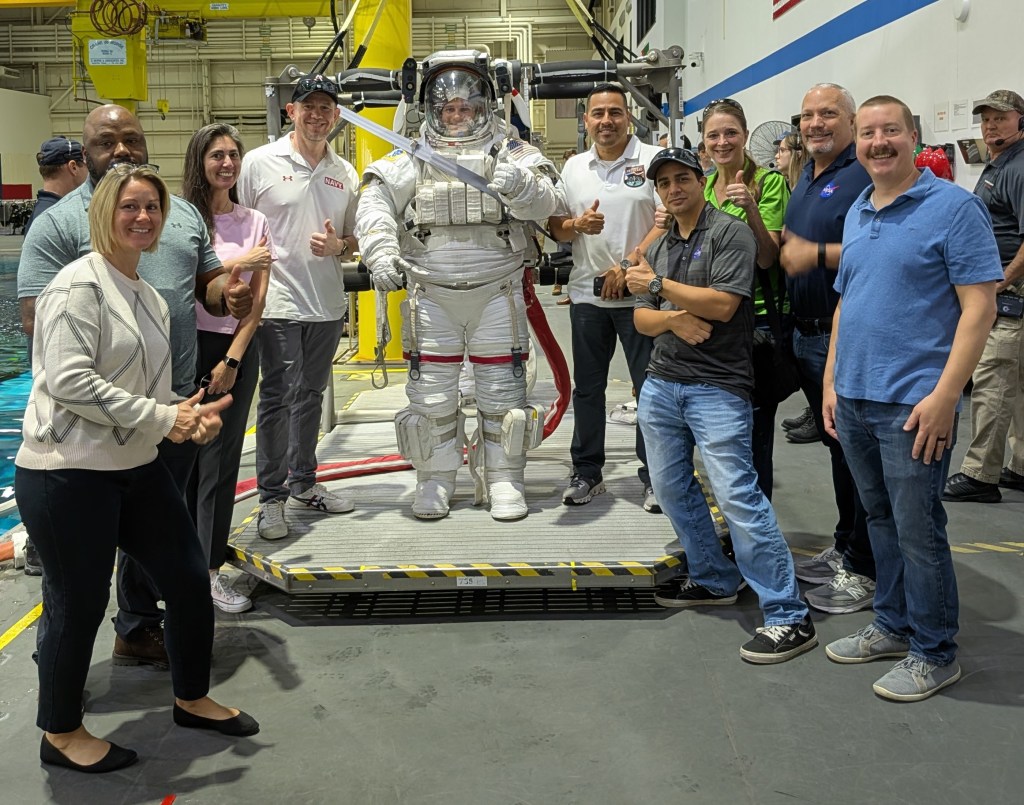 Group photo of NASA SkillBridge employees around an Astronaut suit at the JSC Neutral Buoyancy Laboratory.