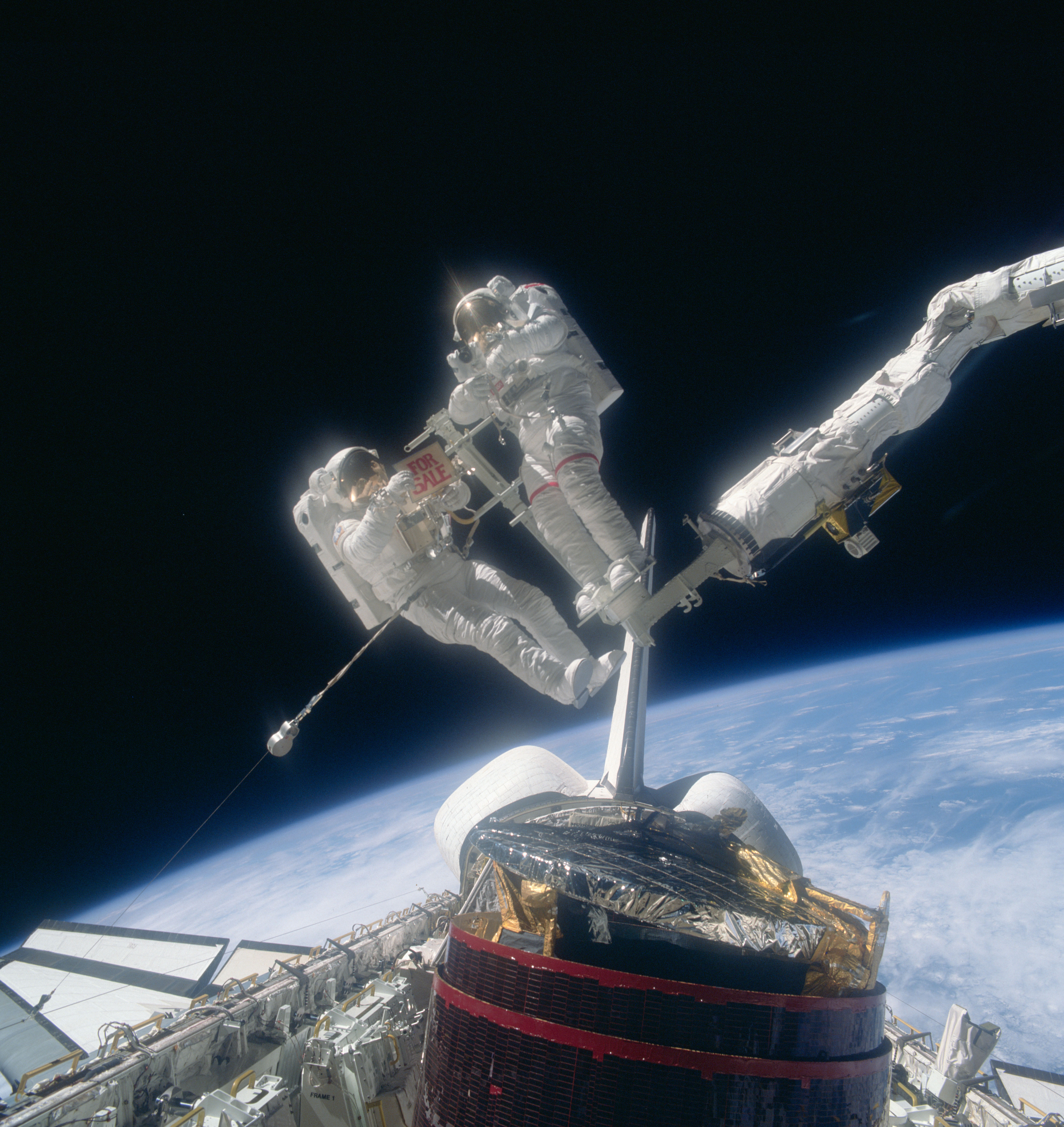 Dale A. Gardner and Joseph P. Allen pose at the end of the Remote Manipulator System controlled by Anna L. Fisher