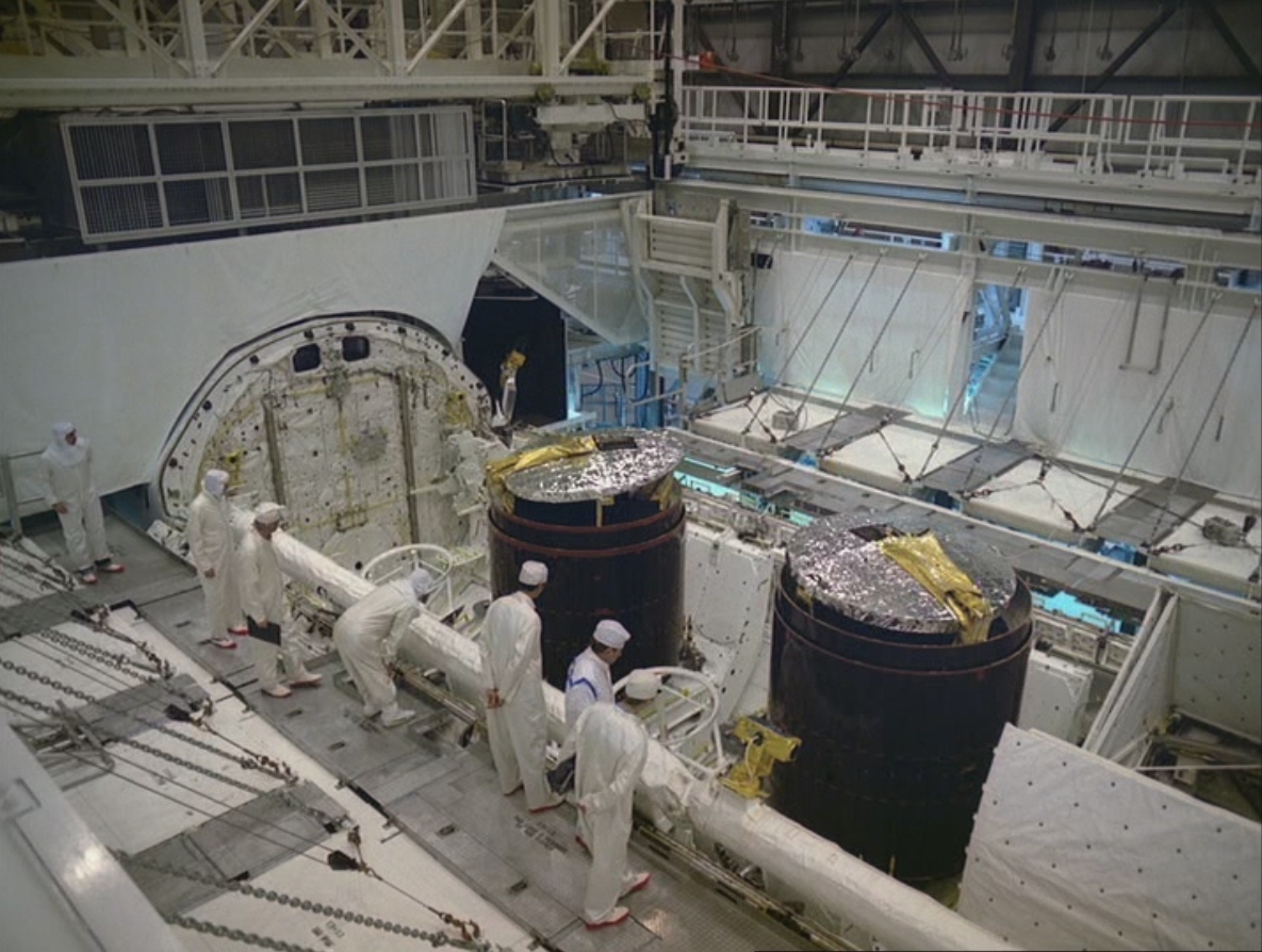 Workers inspect the Westar 6, left, and Palapa B2 satellites in Discovery’s payload bay