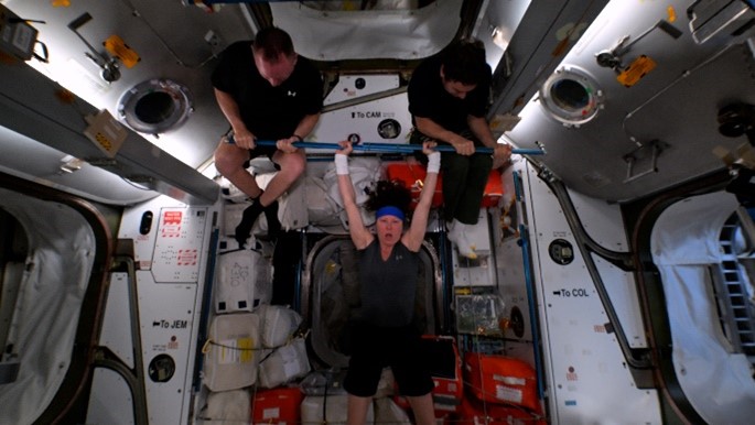 NASA astronaut Tracy C. Dyson powerlifts two of her fellow astronauts during the ISS Olympics.