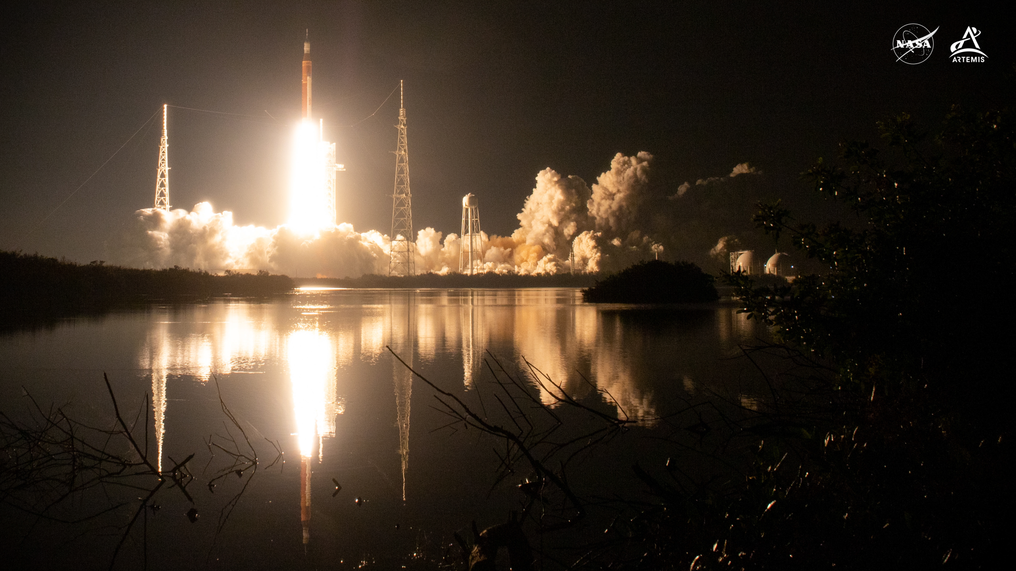 Framed by vegetation in the foreground and against the backdrop of a black night sky, NASA’s SLS (Space Launch System) rocket carrying the Orion spacecraft launches on the Artemis I flight test on Nov. 16, 2022, from Launch Complex 39B at NASA’s Kennedy Space Center in Florida.