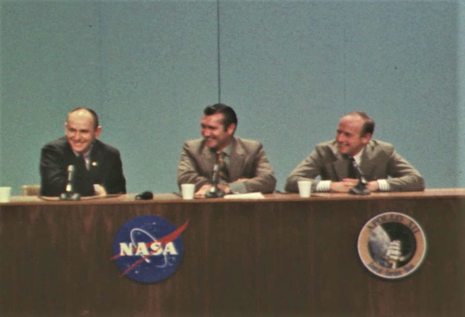 Three men in suits sitting at a podium, giving a press conference.