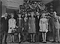 Black and white image of a group of people standing in front of a large Christmas tree.