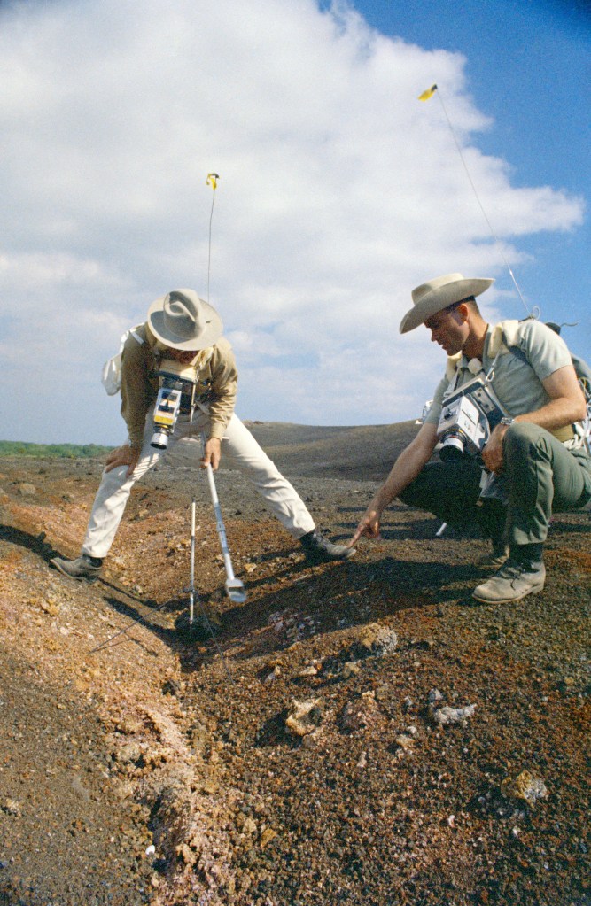 One man standing and another kneeling over a ditch, taking rock and soil samples