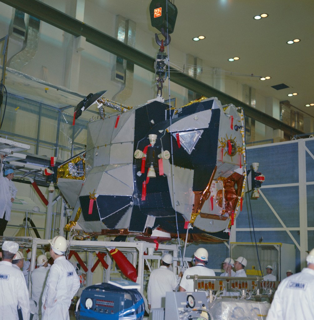 A group of men standing around a spacecraft suspended on a crane