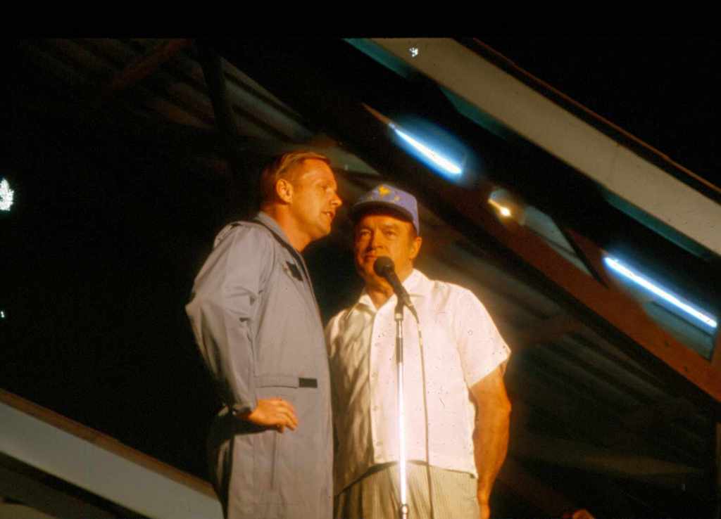 Two men, Neil Armstrong and Bob Hope, standing on stage at a microphone.