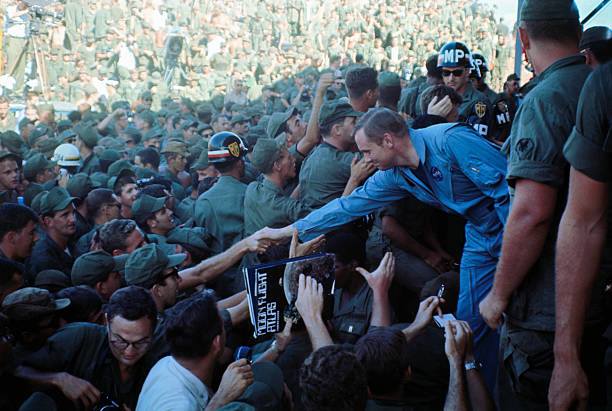 Apollo 11 astronaut Neil Armstrong is surrounded by a large group of soldiers at an outdoor arena, shaking hands with the troops.