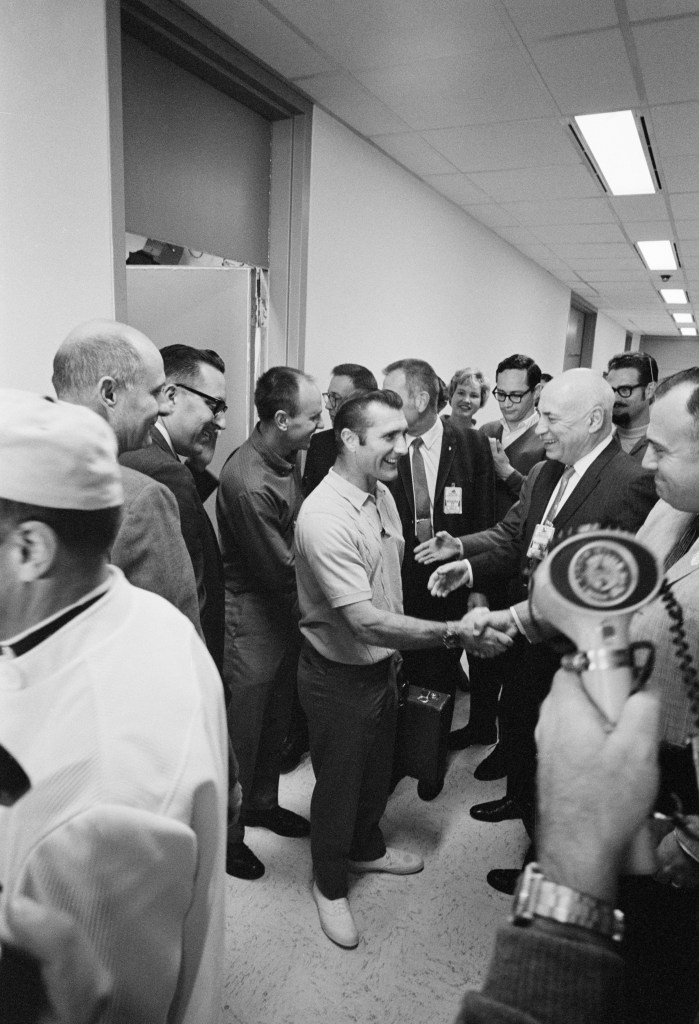 Black and white image of two men shaking hands, surrounded by a group of men