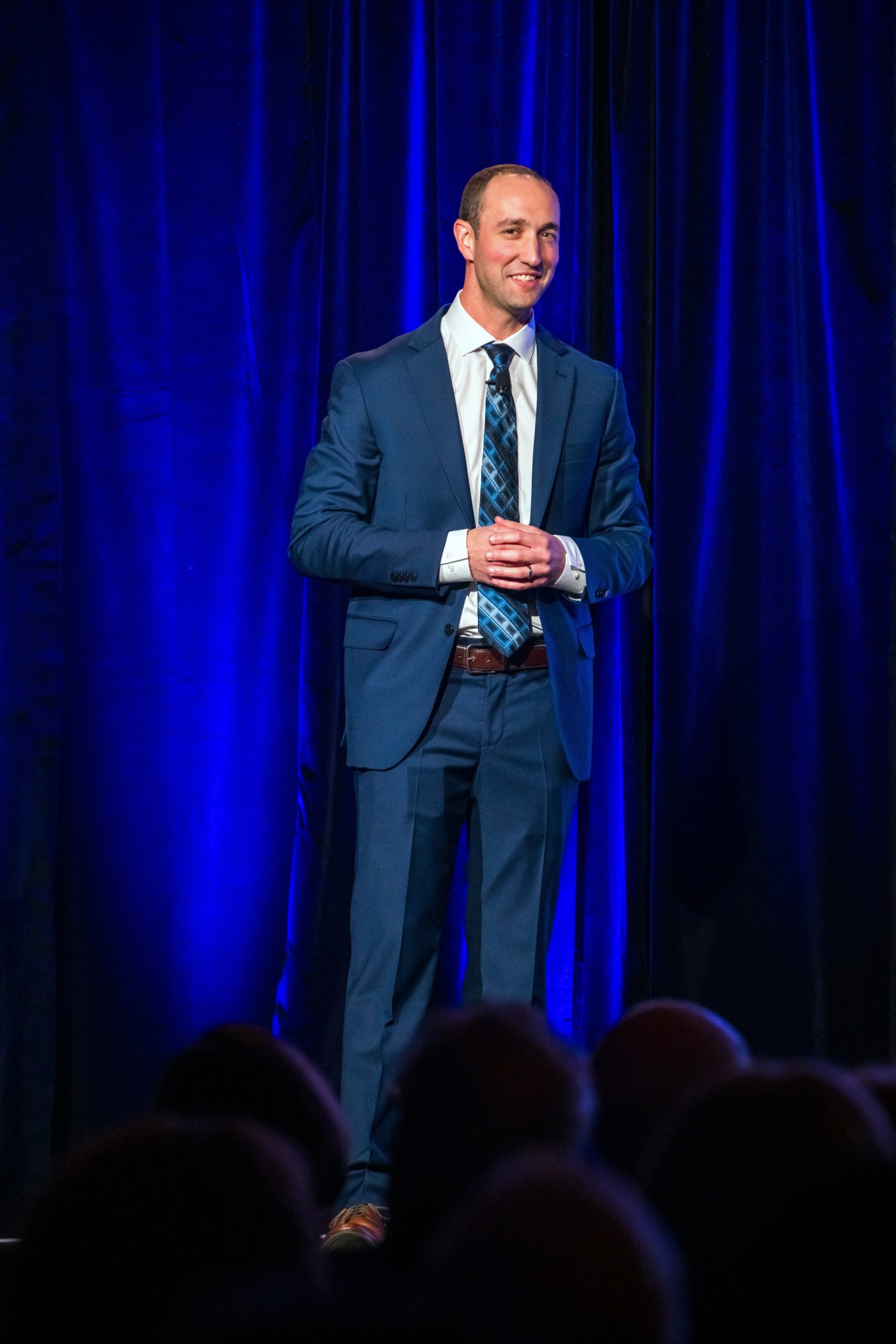 Presenter stands in front of a blue curtain and addresses audience.