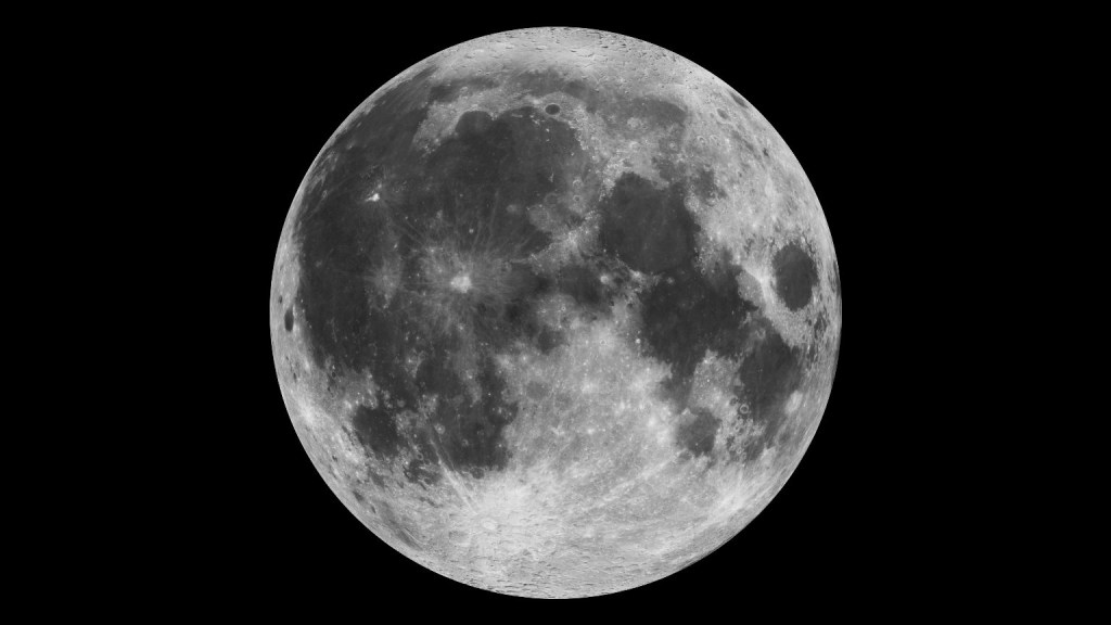 The full Moon stands our against the blackness of the night sky. The Moon appears as a white and gray orb dimpled with craters and valleys.