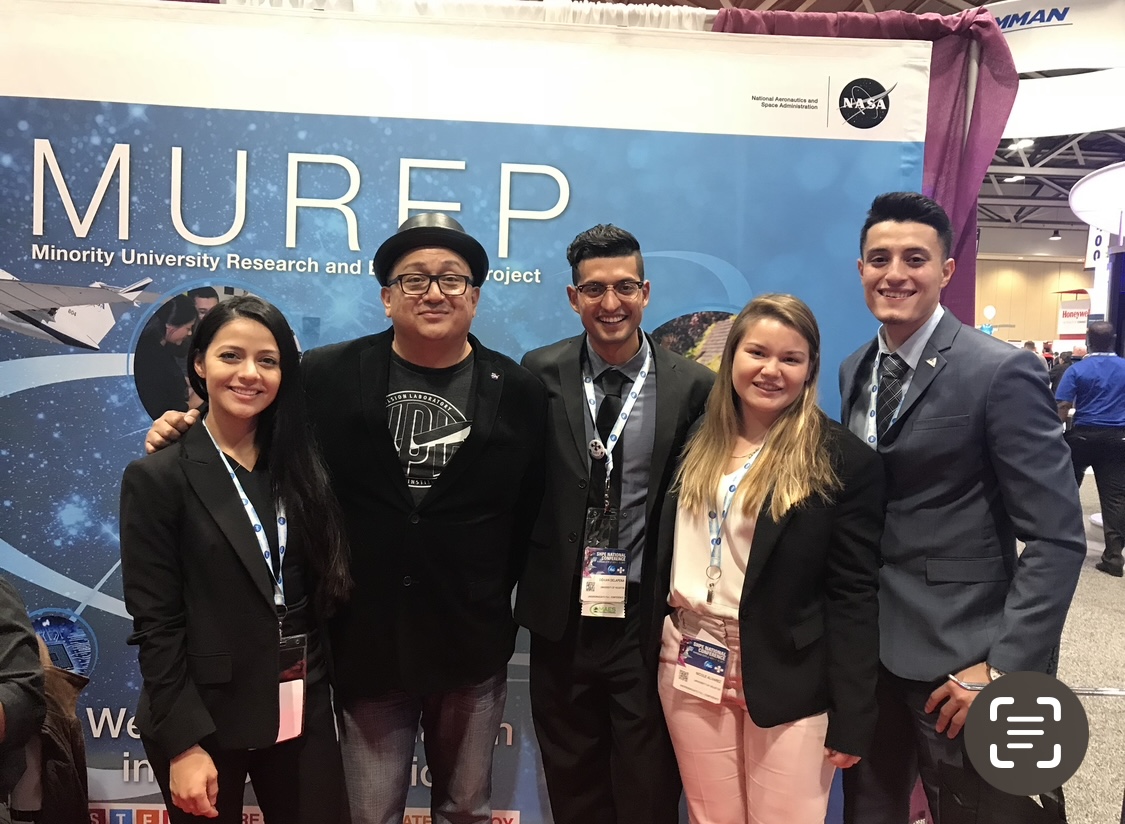 Eddie Gonzales poses with a group of four people with the MUREP, Minority University Research and Education Project, banner behind them.