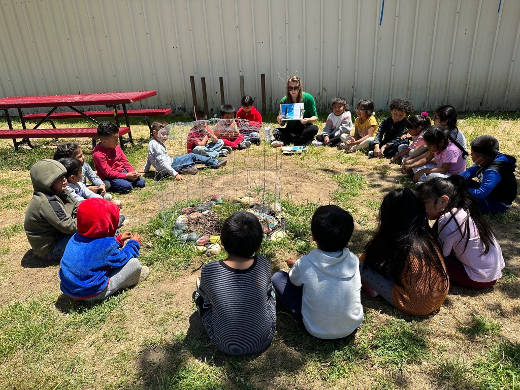 Children sitting in a circle around a newly planted Moon tree and learning about NASA's Artemis I mission.