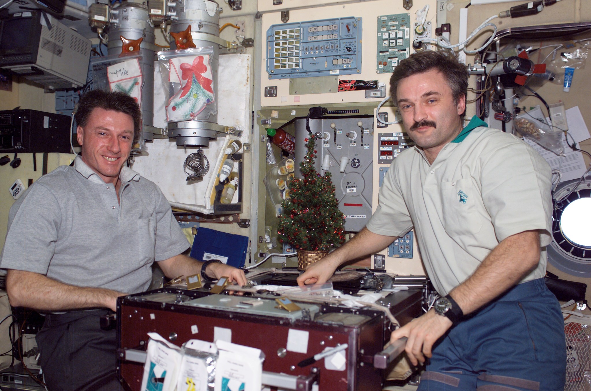 Two men, one in a light blue shirt and the other in tan one, pose for a picture onboard the International Space Station