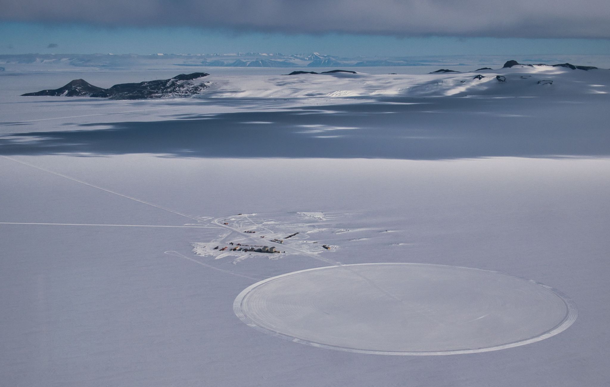 A camp sits outside of a circular launch area carved into the snow-covered landscape of Antarctica.