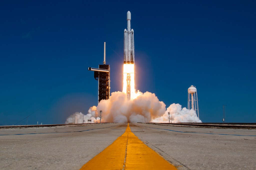 Image shows a rocket lifting off from a launch pad at NASA's Kennedy Space Center