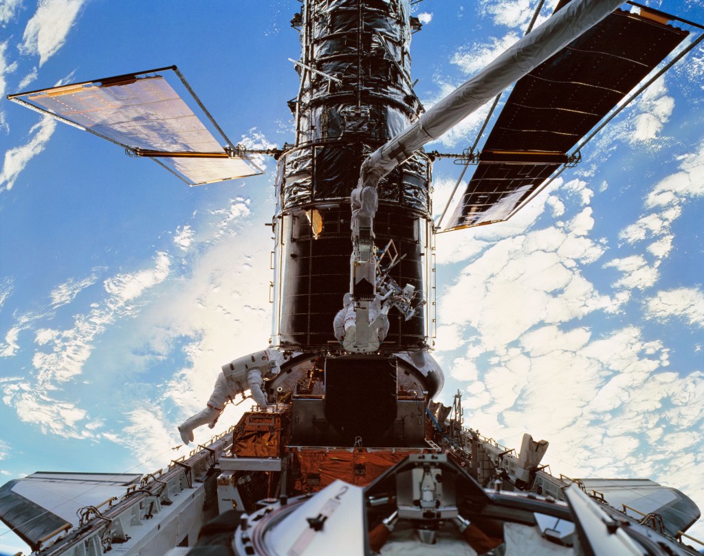 Two astronauts in white spacesuits work on the Hubble Space Telescope