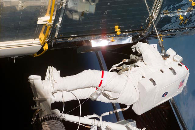 An astronaut clad in a white spacesuit conducts a spacewalk at the Hubble Space Telescope