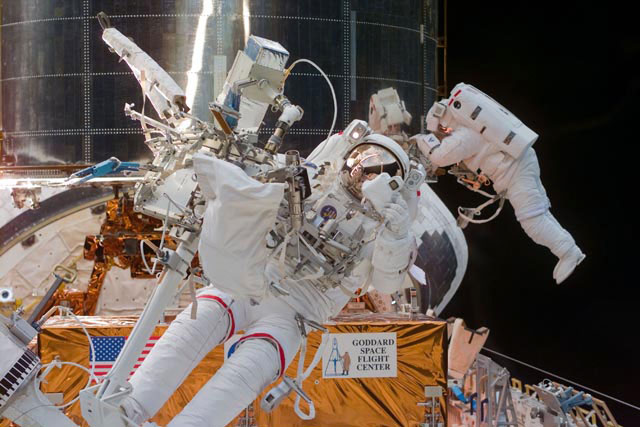 Two astronauts wearing white spacesuits during a spacewalk to repair the Hubble Space Telescope