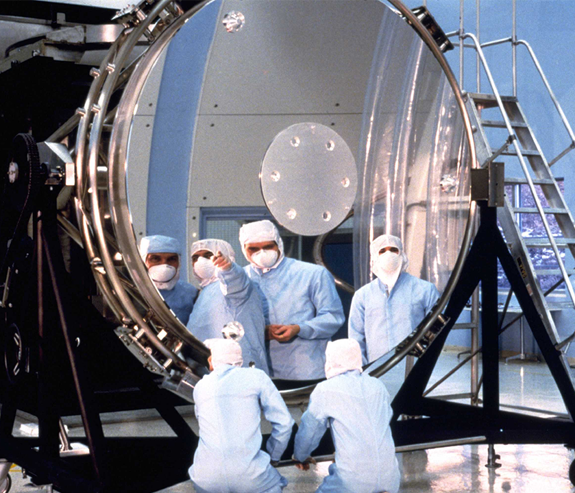 A group of technicians in bunny suits reflected in the Hubble's primary mirror