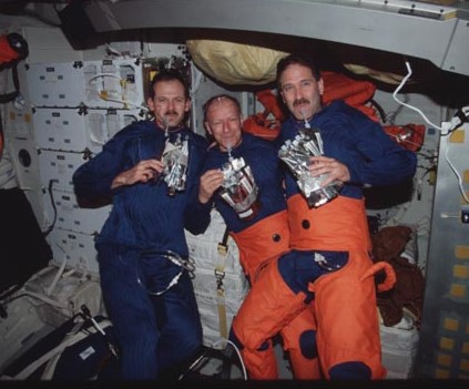 Three astronauts floating side by side holding drink bags