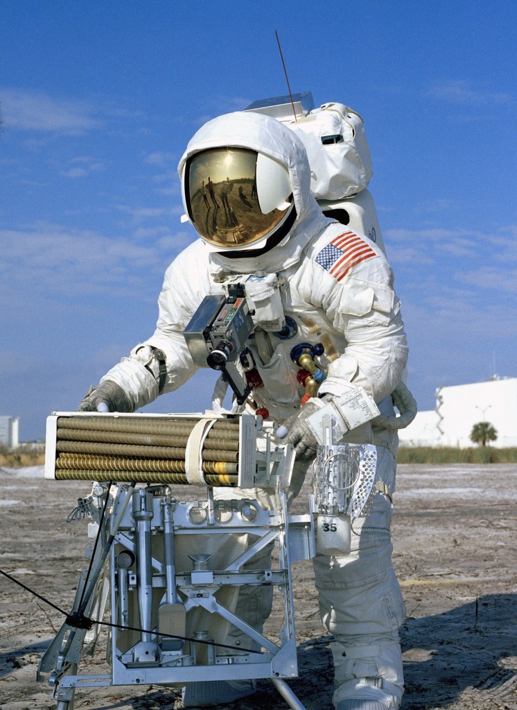 An astronaut clad in a white spacesuit and a helmet with a reflective visor is working outside.